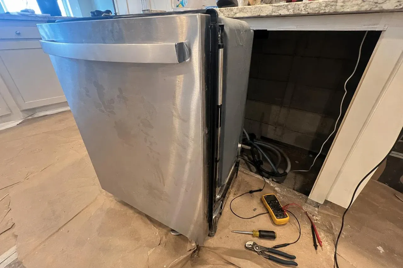 Technician's dishwasher pulled out for diagnosis with a multimeter and tools on the floor